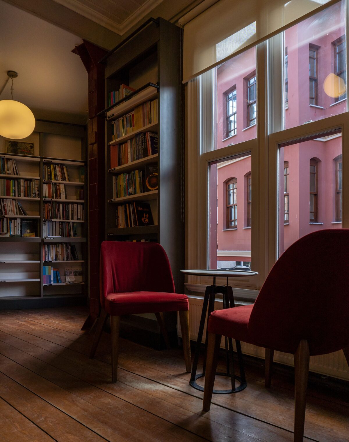 Reading corner with bookshelves, two red chairs and a small table by a tall window